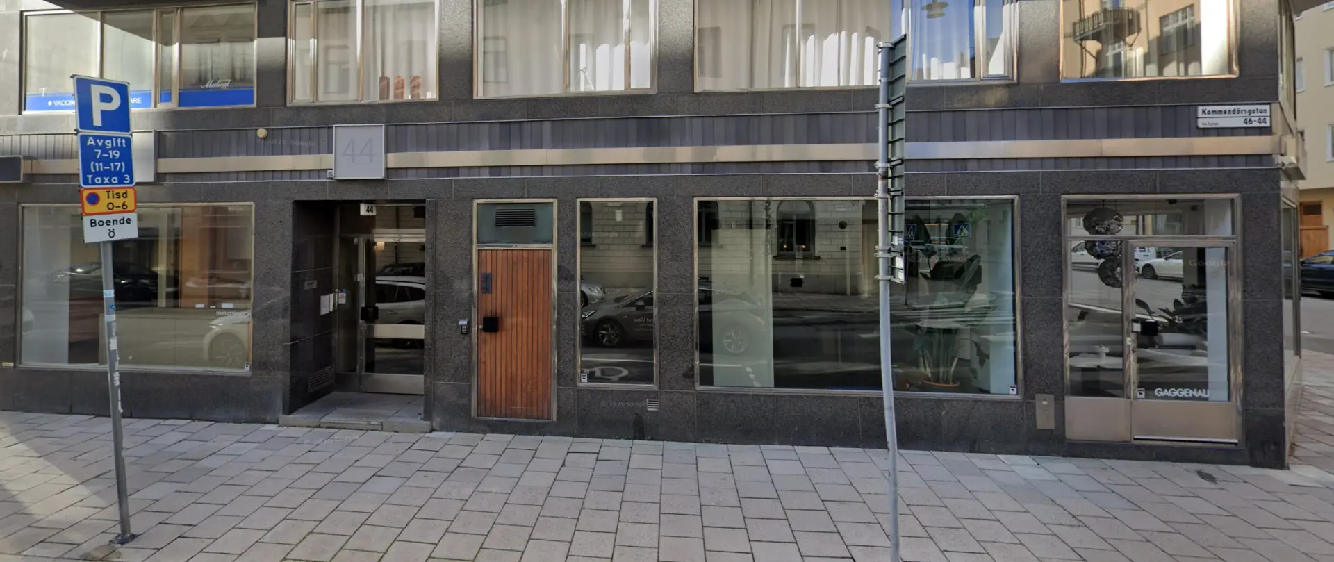 Entrén på Kommendörsgatan 44: glasdörr med nummer 44 i mörk granitfasad, till vänster om en trädörr